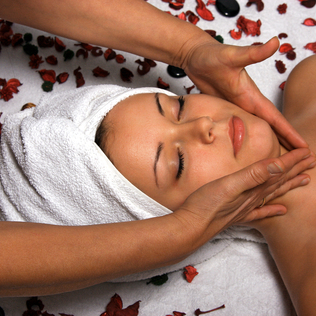 Eine Frau erhält eine Gesichtsmassage mit Rosenblättern und Steinen um sie herum.